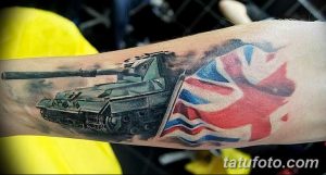 Фото тату на руке с изображением британского танка и развевающегося флага Великобритании. Реалистичный стиль, детализированная проработка, патриотический дизайн.