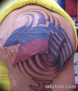 Фото тату с изображением шляпы и флага на плече, выполненное в ярких цветах с использованием синего, красного и белого. Рисунок выглядит объемно и реалистично.
