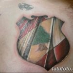 Фото тату герба Ливана на груди, выполненное в ярких цветах с использованием красного, зеленого, белого и черного. Детализированный рисунок с изображением кедра.