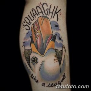 Фото тату: яркая татуировка чайки с надписью "Squawk like a seagull" на предплечье, в стиле олдскул, красочный рисунок татуировки.