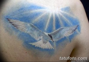 Фото акварельной татуировки с изображением белого голубя, летящего в небе. Рисунок выполнен в голубых и белых тонах.