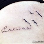 Фото минималистичной татуировки с надписью 'Luciana' и изображением летящих птиц на плече. Черно-белый рисунок татуировки.
