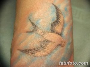 Фото минималистичного тату летящей птицы на запястье. Небольшой рисунок татуировки в черно-серых тонах.
