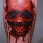 Фото тату на руке, изображающее череп, из которого стекает кровь. Выполнено в реалистичном стиле с использованием темных и красных цветов.