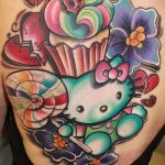 Фото татуировки на теле: Hello Kitty с разбитым сердцем, окруженная цветами и яркими элементами в стиле old school.