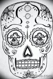 Фото тату черепа в стиле сахарной смерти (Calavera), украшенного сложными узорами и цветочными элементами. Черно-белый рисунок.