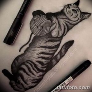 Фотография реалистичной черно-белой татуировки, изображающей кошку, уютно свернувшуюся рядом с клубком ниток. Детализированная прорисовка создает эффект присутствия.