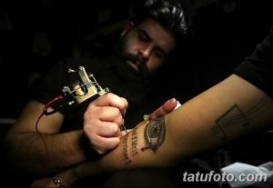 Фото тату: Мастер тату делает татуировку на руке клиента. Видна тату-машинка, рука клиента и рука мастера.
