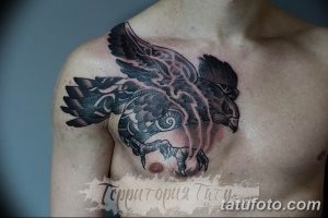 Фото тату ворона на груди с элементами дыма и племенных узоров. Черно-серый рисунок татуировки с динамичной композицией.