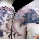 Фото тату ворона, сидящего на ветке дерева на плече. Черно-серый рисунок в стиле реализм с детальной проработкой коры дерева и перьев птицы.