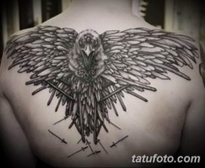 Фото тату ворона с костями на спине, выполненного в стиле dark art. Мрачный и загадочный рисунок татуировки с использованием черного цвета и тонких линий.