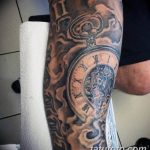 Черно-серое фото тату на руке, изображающее сложные часы с механизмами и узорами. Стиль олдскул с четкими линиями и насыщенными цветами.