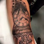 Черно-серое фото тату на предплечье с изображением часов и летящих птиц. Детализированный рисунок с использованием теней и градиентов.