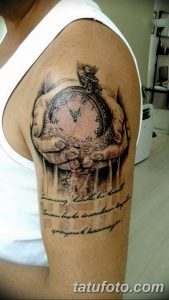 Фото тату: черно-серая татуировка песочных часов, окруженных облаками и перьями, на плече. Романтичный и загадочный дизайн.