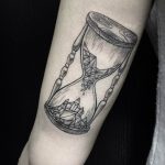 Фото тату: черно-белая графическая татуировка с изображением песочных часов, наполненных геометрическими фигурами. Стильный и минималистичный рисунок.