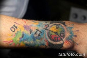 Фото тату часы на запястье, выполненные в акварельном стиле с яркими брызгами красок и цифрами, символизирующими хаотичное течение времени.
