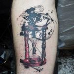 Фото тату на ноге: песочные часы с текущим песком и размытыми линиями. Оригинальный рисунок в черно-белых тонах.