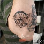Черно-серое фото татуировки на локте, изображающей старинные часы и ключ. Детализированный рисунок с брызгами краски.