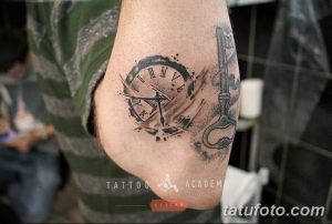 Черно-серое фото татуировки на локте, изображающей старинные часы и ключ. Детализированный рисунок с брызгами краски.