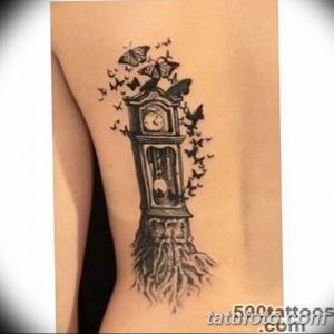 Фото татуировки старинных напольных часов, из которых вылетают бабочки, на женской ноге. Черно-серый рисунок татуировки выполнен в реалистичном стиле.
