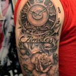 Фото тату на руке: карманные часы, розы и надпись "Timeless" в черно-белом стиле.