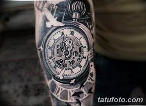 Черно-серое фото тату карманных часов с летящими птицами на предплечье. Детализированный рисунок с элементами механики и легкими мазками.