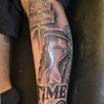 Фотография татуировки на руке с изображением песочных часов и надписи 'Time Alone'. Черно-серые тона, реалистичный стиль.