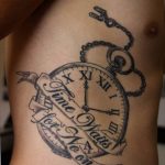 Фото тату на боку с изображением карманных часов и надписи "Time waits for no one". Черно-серый рисунок с элементами декора.