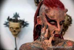 Фотография мужчины с экстремальными модификациями тела, включая татуировки, пирсинг и шрамирование. Яркий и провокационный образ.