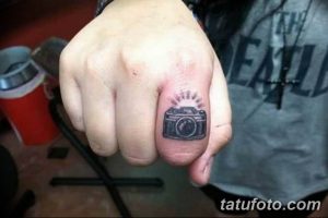 Фото тату на пальце: крошечный фотоаппарат, выполненный в черном цвете, с небольшими деталями и бликами света.