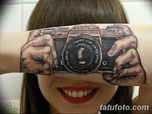 Фото тату с изображением старинной камеры Pentax, словно держащейся в руке. Высокодетализированный и реалистичный рисунок на руке девушки.
