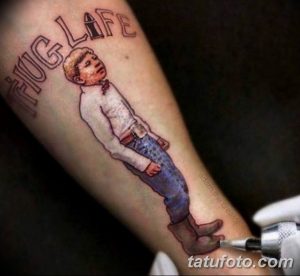 Фото татуировки на руке с изображением мальчика в костюме и надписью 'Fug Life', выполненное в ярких цветах.