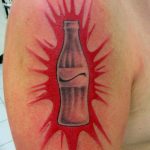 Яркая татуировка на плече с изображением бутылки Coca-Cola, из которой вырываются красные брызги. Динамичный и оригинальный дизайн.
