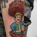Фото татуировки на предплечье с изображением персонажа из игры Fallout и яркого ядерного взрыва в стиле комиксов.