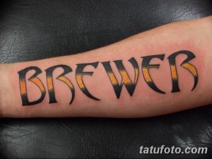 Фото тату надписи 'BREWER' на предплечье, выполненной в ярких оранжево-черных тонах с золотой обводкой. Стильная и современная татуировка.