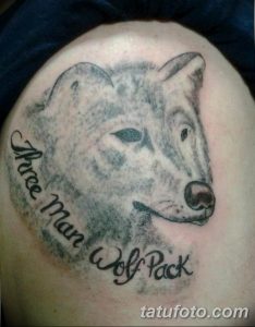Фото тату на плече мужчины, изображающее голову волка и надпись 'Three Man Wolf Pack'. Выполнено в реалистичном стиле, с использованием черно-серых тонов.