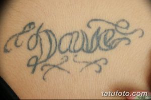 Фото тату надписи "Dave" на груди в каллиграфическом стиле. Изящные линии, декоративные элементы, сине-серые тона.