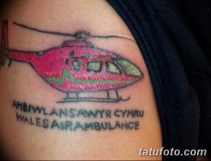 Фото тату на плече: изображение вертолета скорой помощи с надписью 'Ambulwlans Cymru Wales Air Ambulance'. Рисунок татуировки в ярких цветах.