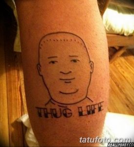 Фото тату на предплечье: карикатурный портрет мужчины с надписью 'Thug Life'. Черно-белый рисунок татуировки в минималистичном стиле.