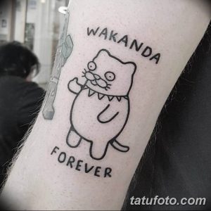 Фото тату: мультяшный кот с зубами и надписью 'Wakanda Forever' на руке, выполненный в черном цвете в стиле аниме.