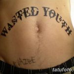 Фото тату надписи "Wasted Youth" на животе. Черный цвет, готический шрифт.