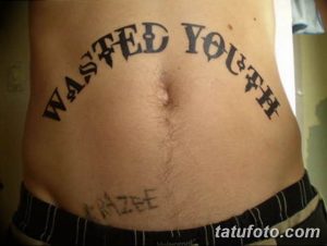 Фото тату надписи "Wasted Youth" на животе. Черный цвет, готический шрифт.