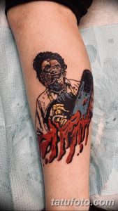 Фото татуировки на ноге с изображением Leatherface из фильма 'Техасская резня бензопилой', держащего бензопилу. Рисунок выполнен в ярких цветах.