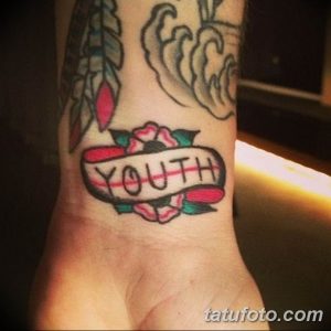 Фото татуировки на запястье с надписью 'YOUTH', обрамленной розами и лентой. Рисунок выполнен в стиле олд скул.