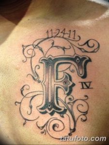 Фото тату стилизованной буквы "F" с датой "11.24.11" и римской цифрой "IV" на груди. Черно-белый рисунок с декоративными элементами.