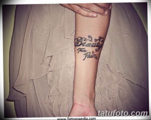 Фото тату надписи "Beauty From Pain" на запястье. Изящный шрифт с декоративными элементами, выполненный в черном цвете.