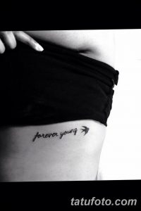 Фото тату надписи 'forever young' на боку. Черный контур, тонкий шрифт, минималистичный дизайн. Идеально для тех, кто ценит простоту и символизм.