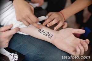Фото процесса нанесения татуировки: мастер переносит трафарет с числовым кодом на руку клиента.
