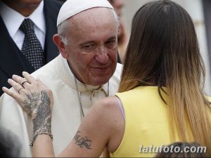 Фотография Папы Римского Франциска, обнимающего девушку с видимыми татуировками на руках. Татуировки выполнены в стиле традиционной графики.