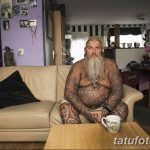 Фотография пожилого мужчины с татуировками на теле, сидящего на диване в домашней обстановке, демонстрирующая его индивидуальность и любовь к искусству.